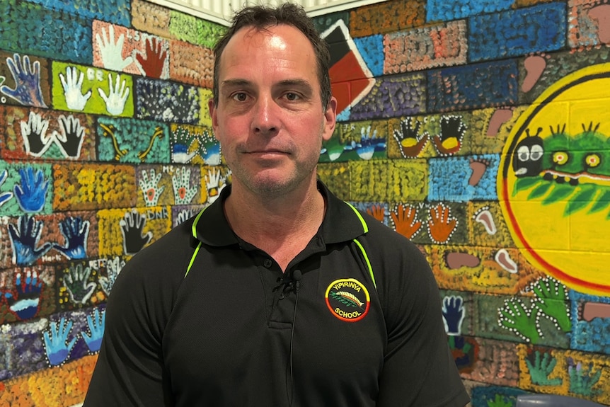 A man standing in front of a wall decorated with hand-prints and aboriginal-style paintings